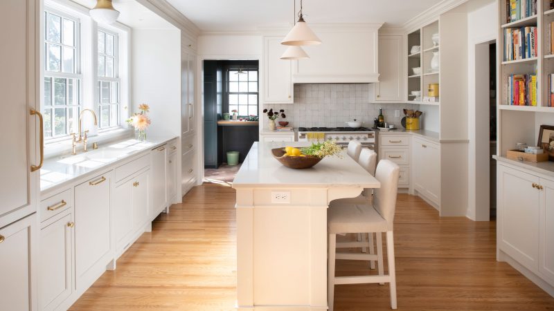 Bright kitchen with white cabinets and walls, a kitchen island with chairs, and hardwood floors